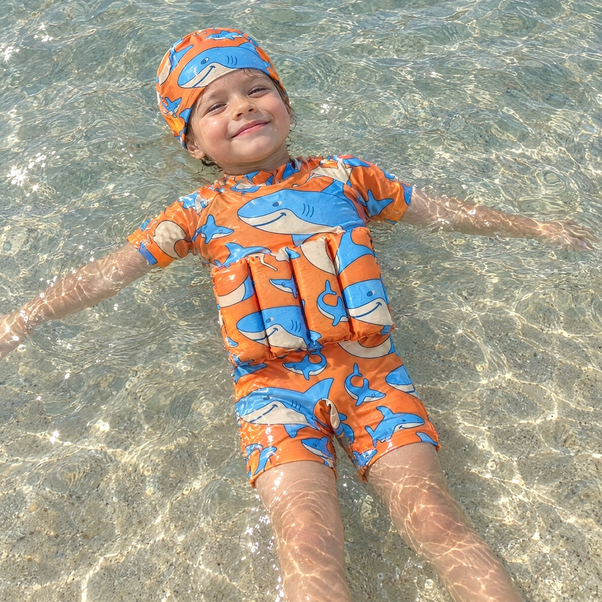 A child floating in the ocean wearing an orange SafePlouf wetsuit